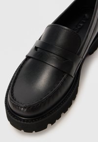 Mustad nahast loaferid, millel on sile ülemine osa, dekoratiivne riba ees ja tekstureeritud kummitald, millel on mustriga tallaosa.