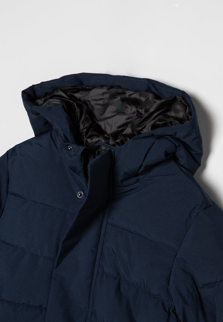 Chaqueta acolchada de color azul marino con capucha desmontable, que presenta un diseño acolchado, botones a presión y un forro negro suave.