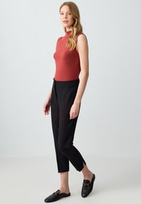 Rode mouwloze top, getailleerd ontwerp, gecombineerd met zwart hoge taille tailleurs, en zwarte instap schoenen met accenten van goudkleurig beslag.
