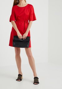 Vestido rojo de manga corta con cintura ceñida, combinado con un bolso de mano negro y sandalias destalonadas con detalles de flecos y un patrón a rayas.