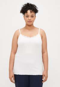 Camisola branca canelada com alças ajustáveis e bordo de renda na gola, apresentando uma bainha assimétrica e uma textura suave.