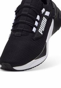 Zapatilla deportiva negra con parte superior de malla texturizada, acentos blancos, logo de Puma prominente y suela de goma duradera.