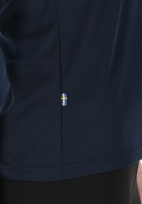Maglietta sportiva blu navy con tessuto testurizzato. Presenta un piccolo accento della bandiera svedese sul retro, vicino all'orlo.