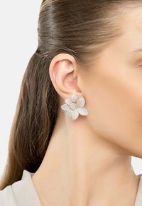 Sparkling silver-tone floral earrings with petal-shaped designs, embellished with small gems, attached to a model's ear.