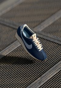 Tamno plavaške atletske cipele od kombinacije antilopa i mrežastih materijala, boje kremastih vezica, bijeli Swoosh logo i teksturirana gumena potplata.