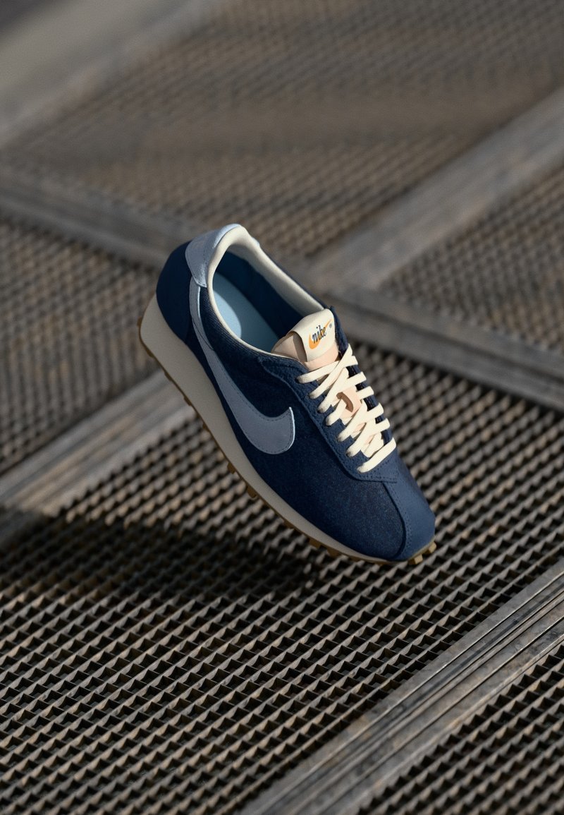 Tamno plavaške atletske cipele od kombinacije antilopa i mrežastih materijala, boje kremastih vezica, bijeli Swoosh logo i teksturirana gumena potplata.