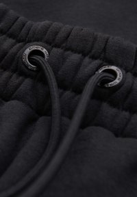Gros plan d'une ceinture élastique noire avec deux cordons noirs passés dans des œillets métalliques sur un vêtement en tissu.