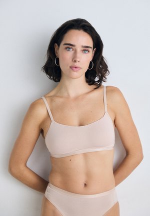 Nude bralette with thin straps and a smooth, seamless design. The fabric appears soft and stretchy, with a matching brief displayed.