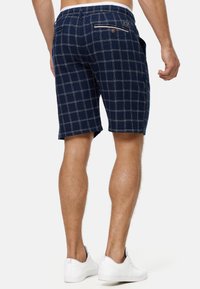 Pantalones cortos a cuadros en azul marino, fabricados en tejido ligero, con cintura con cordón, bolsillos traseros y acentos de costuras blancas.