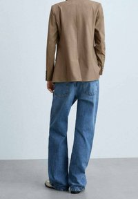 Brown tailored blazer, denim jeans, and light shoes. Blazer features a fitted design with a smooth texture; jeans are loose-fitting with pockets.