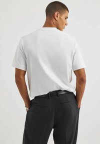 Biała koszulka z krótkim rękawem i okrągłym dekoltem, o luźnym kroju. Połączona z dopasowanymi czarnymi spodniami, które mają tylne kieszenie.