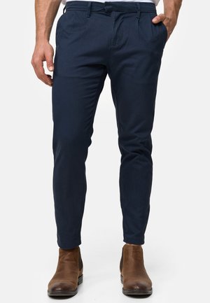 Granatowe chinosy wykonane z gładkiego materiału, slim fit z płaskim przodem, z kieszeniami po bokach, w zestawieniu z brązowymi botkami za kostkę.