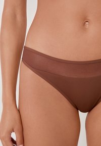 Fondo di bikini marrone con una texture liscia e semitrasparente. Presenta una vita sottile e un design minimalistico, adatto a diverse taglie.