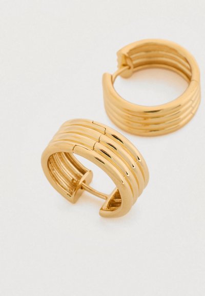 Χρυσά σκουλαρίκια κρίκοι με ανάγλυφο σχεδιασμό και μεντεσέ κλεισίματος. Η επιφάνεια είναι λαμπερή με λεία υφή και ομοιόμορφο χρώμα.