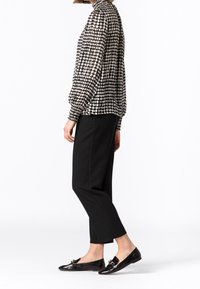 Blusa a motivi in bianco e nero con colletto alto e polsi elasticizzati, abbinata a pantaloni neri a sigaretta e scarpe basse nere lucide con dettaglio a fiocco.