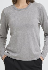 Pull gris à manches longues avec un col rond, fabriqué en matière douce et légère. Présente une silhouette ajustée et des poignets côtelés.