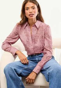 Sheer pink blouse with textured stripes, long sleeves, and buttons. Paired with high-waisted blue wide-leg jeans.
