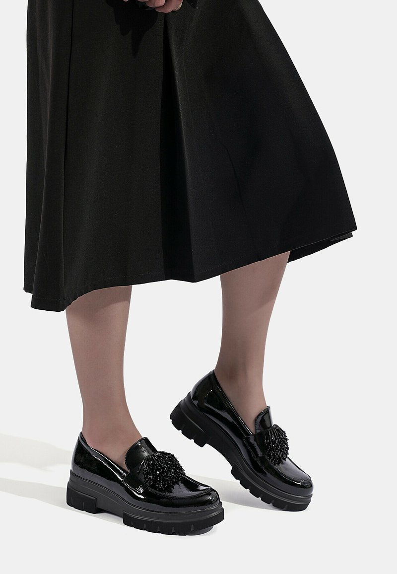 Mocassini in vernice nera con suola in gomma spessa e un accent pom-pom testurizzato sulla parte anteriore. Finitura liscia, design a bassa scollatura.
