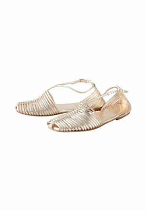 Silverfärgade metalliska platta sandaler med öppen tå, som har tunna vertikala remmar, ett justerbart ankelsnörning och en minimalistisk design.