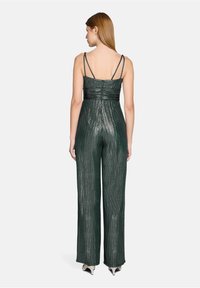 Combinaison verte métallique avec un corsage ajusté, des bretelles fines, des plis horizontaux et un pantalon à jambes larges. Surface texturée avec un effet scintillant.