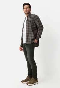 Plaid button-up shirt in brown, blue, and orange tones, worn over a white t-shirt. Paired with dark green slim-fit pants and brown sneakers.