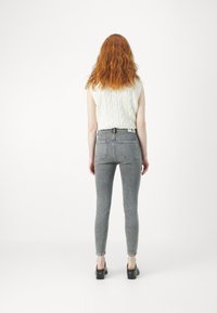 Grå tajta jeans med hög midja, bakfickor och en figurnära silhuett, i kombination med en krämfärgad ribbad stickad ärmlös topp.