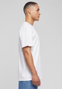 Hvid bomulds T-shirt med korte ærmer, rund halsudskæring og en afslappet pasform. Modellen har lyseblå jeans på.