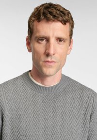 Szary, teksturowany sweter dzianinowy z wzorem w zygzak i prążkowanym dekoltem, w połączeniu z jasnym podkoszulkiem.