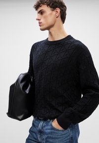 Maglione nero a maglia con un motivo a diamante texture, collo rotondo e maniche lunghe. Abbinato a una borsa in pelle nera e jeans blu.