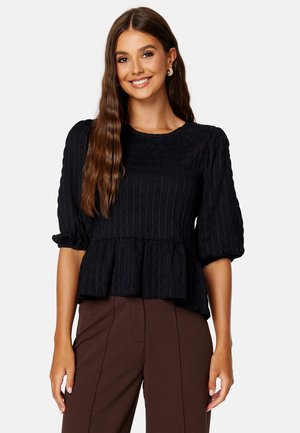 Top peplum nero testurizzato con maniche puff a tre quarti e scollatura rotonda, abbinato a pantaloni sartoriali marroni.