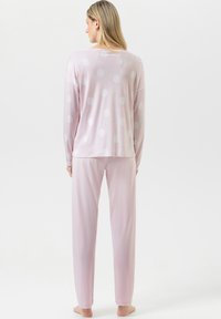 Ensemble de pyjama rose clair comprenant un haut à manches longues avec des pois blancs et un pantalon assorti. Tissu doux avec une coupe décontractée.