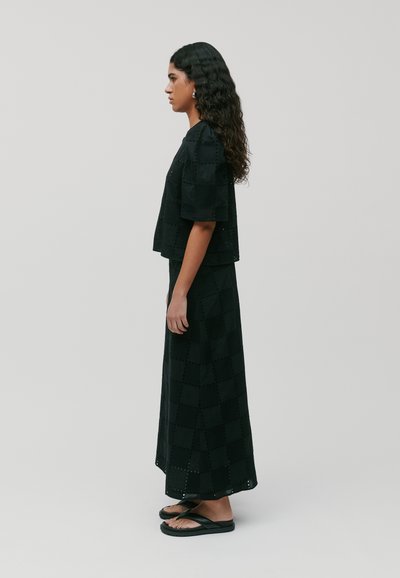 Top corto nero con pattern testurizzato, abbinato a una lunga gonna nera con un design simile, indossato con infradito nere.
