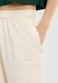 Crème kleurige joggers met een elastische tailleband, zijzakken en een ritszak. Heeft subtiele reliëfbranding op de dij.