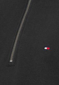 Μαύρο φούτερ με γιακά μισής ζώνης, με ασημένιο φερμουάρ και μικρό κεντημένο λογότυπο σε κόκκινο, λευκό και μπλε. Απαλή υφή.