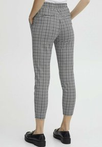 Pantaloni a scacchi in bianco e nero con gamba affusolata, vita elasticizzata, tasche laterali e indossati con scarpe con tacco nero.