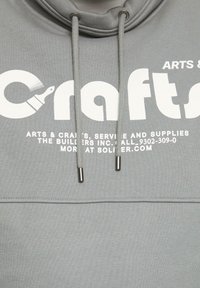 Szary hoodie z dużym białym napisem "Crafts" i grafiką pędzla. Zawiera sznurki z metalowymi końcówkami oraz gładką teksturę.