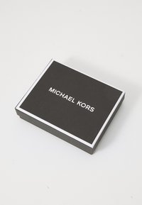 Zwarte doos met een gestructureerde afwerking, witte rand en vetgedrukte witte tekst "MICHAEL KORS" aan de bovenkant. Rechthoekige vorm.