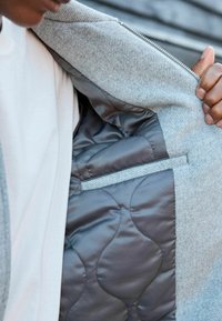 Grijze zip-up jacket met een gewatteerde grijze voering en een zachte textuur. De binnenkant heeft een horizontale zak met een contrasterende bies.