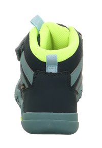 Dětská sportovní obuv s tmavě navy a tyrkysovým syntetickým povrchem, lískově zeleným polstrovaným límcem a nastavitelným popruhem pro bezpečné uchycení.