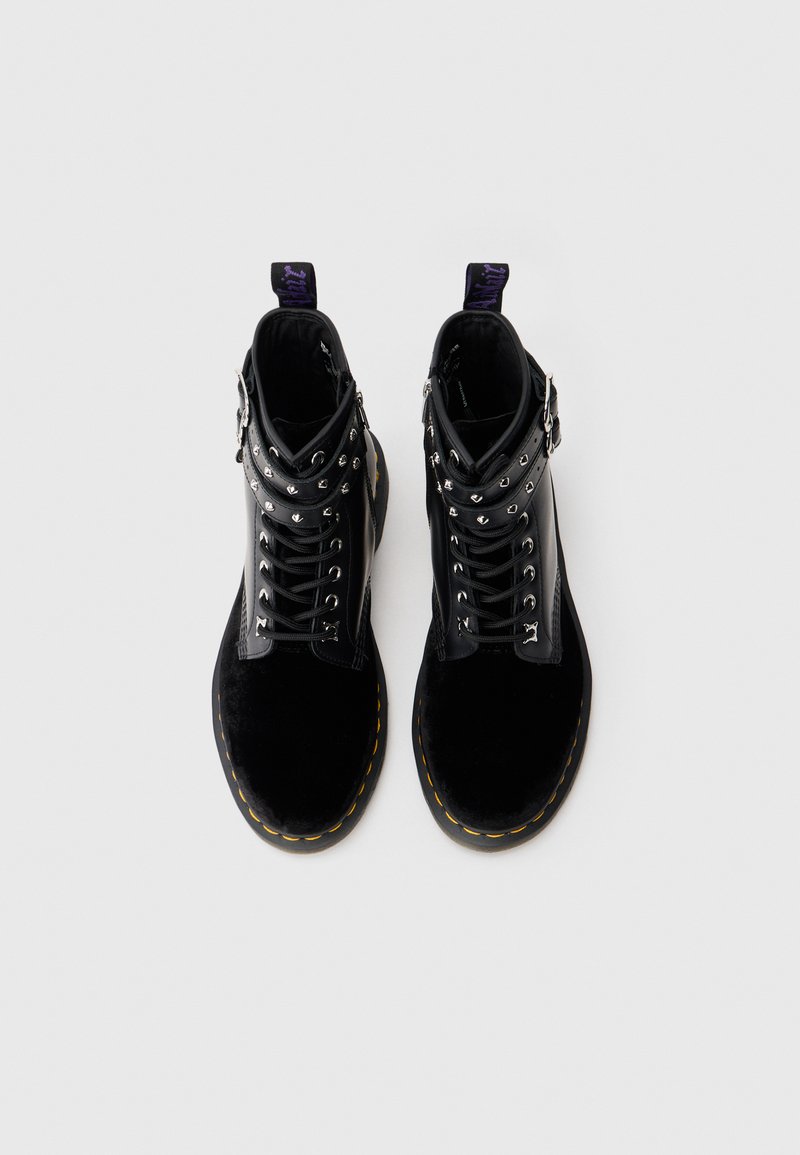 Black ankle boots with a combination of smooth leather and velvet textures. Features metal eyelets, laces, and a contrasting yellow sole.