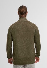 Olive green sweater with a high collar and ribbed cuffs, featuring a textured knit with flecks of light colors throughout.