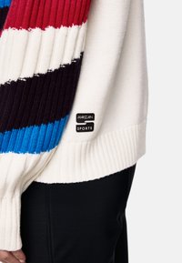 Weißer Strickpullover mit horizontalen Streifen in Rot, Blau, Schwarz und Weiß. Mit einem schwarzen Etikett mit "MARC CAIN SPORTS". Texturiertes Rippbündchen.