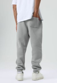 Grijze joggingbroek van zachte stof, met een elastische tailleband, elastische boorden bij de enkels en een zak aan de achterkant, gecombineerd met witte sneakers.