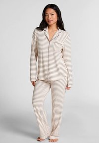 Roomkleurig pyjama-set met horizontale bruine strepen, bestaande uit een overhemd met knopen en een borstzakje, en bijpassende loszittende broek.