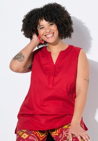 Top rosso senza maniche con scollatura a V e dettagli in pieghe sottili, abbinato a leggins multicolori con fantasie geometriche.