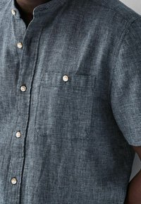 Camicia a maniche corte con bottoni in blu scuro con motivo a quadri e taschino sul petto. Presenta bottoni in legno chiaro e tessuto strutturato.