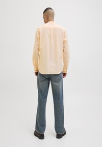 Lichtgele lange mouwen shirt met een rechte zoom, knoopmanchetten en rug yoke detail, gecombineerd met iets losse blauwe denim jeans.