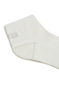 Weißer Baumwollsocken mit gerippter Textur, Knöchellänge, Verstärkung an Ferse und Zehen sowie einem dezenten Markenlabel nahe dem Bündchen.