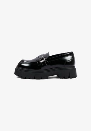 Mocassin en cuir noir avec une semelle en caoutchouc épaisse et un détail de boucle argentée sur le côté, montré de côté extérieur.