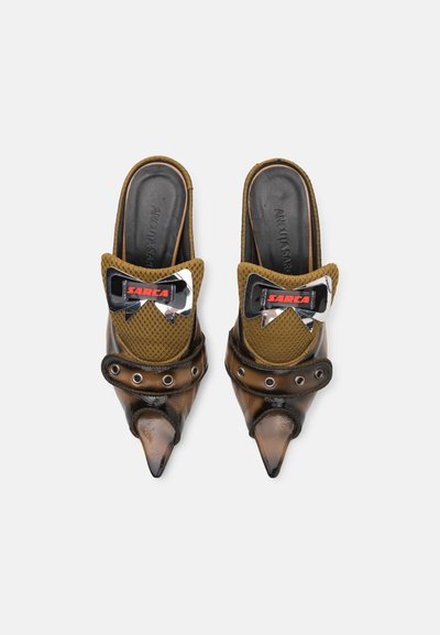 Mules de punta en color marrón y negro con parte superior de malla, plantillas de cuero y un lazo decorativo que presenta un acento en rojo y plata. Incluye detalles de ojales.